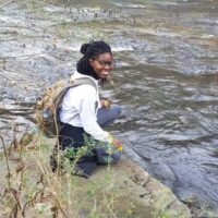 Faith Lyles crouching on a rock near the water